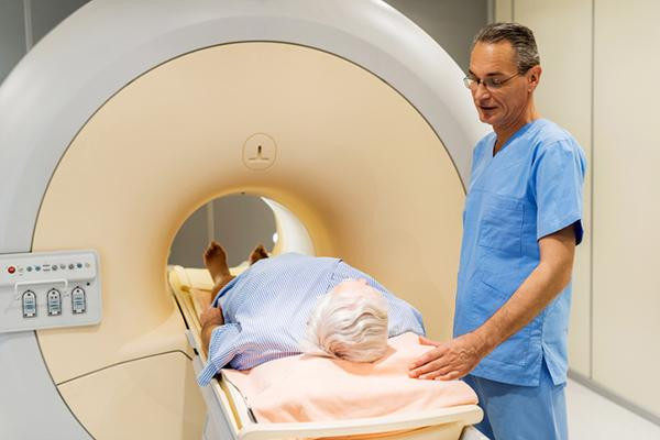 A radiologist in blue scrubs speaks to a patient who is about to be sent into an M R I machine for a scan.